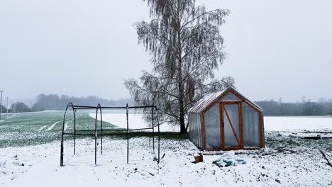 Homestead-greenhouse-in-garden-during-sudden-snowstorm-in-April,-Latvia