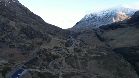 winding road through the rugged terrain of skye with snow-capped mountains in the backdrop, dusk light, aerial view
