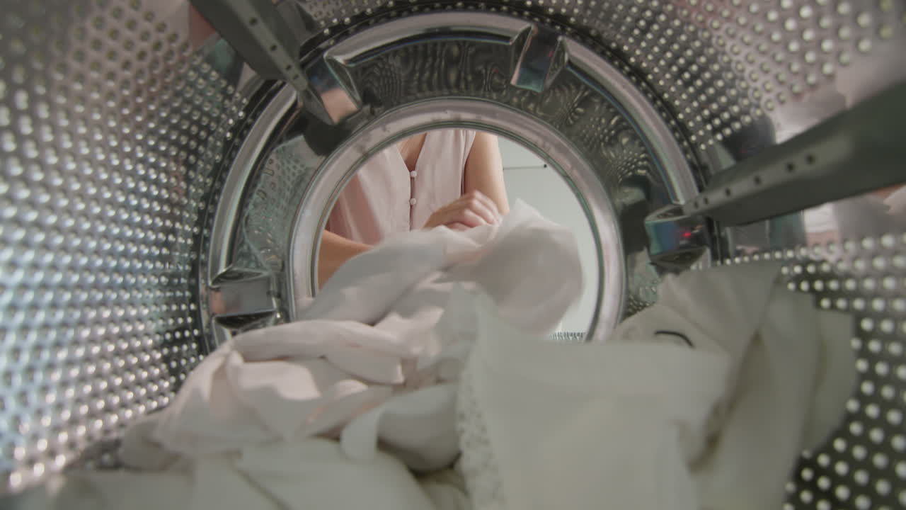 여자는 세탁기에서 세탁된 흰색 리넨을 집어든다