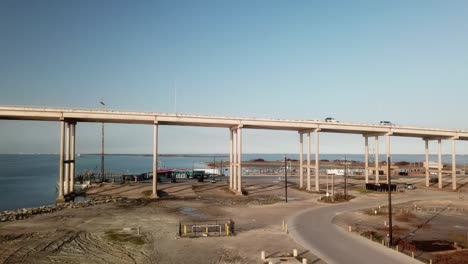 Aerial-reveal-of-the-JFK-Memorial-Causeway-Bridge,-parking-lot,-marina-and-small-storm-islands-in-Laguna-Madre-nearing-sunset-at-North-Padre-Island