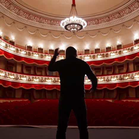 back view of actor on stage. man practicing speech with gestures in empty auditorium with red chairs. performer is reheases in theater