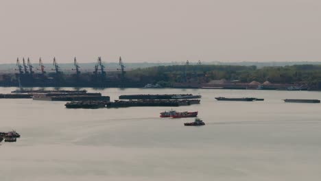 descending drone revealing the two ferries passing by and the industrial backdrop with tall cranes and sturdy stationary barges across the water