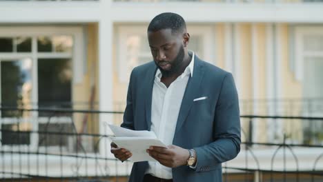 afro businessman examining documents outdoor. focused african man looking papers
