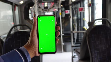 person holding a smartphone with green screen in a bus