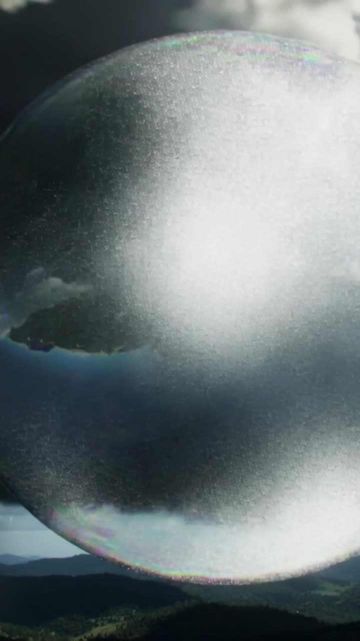 Vertical video: Gliding soap bubble nearing camera on hills, camera zooming causing bright flash