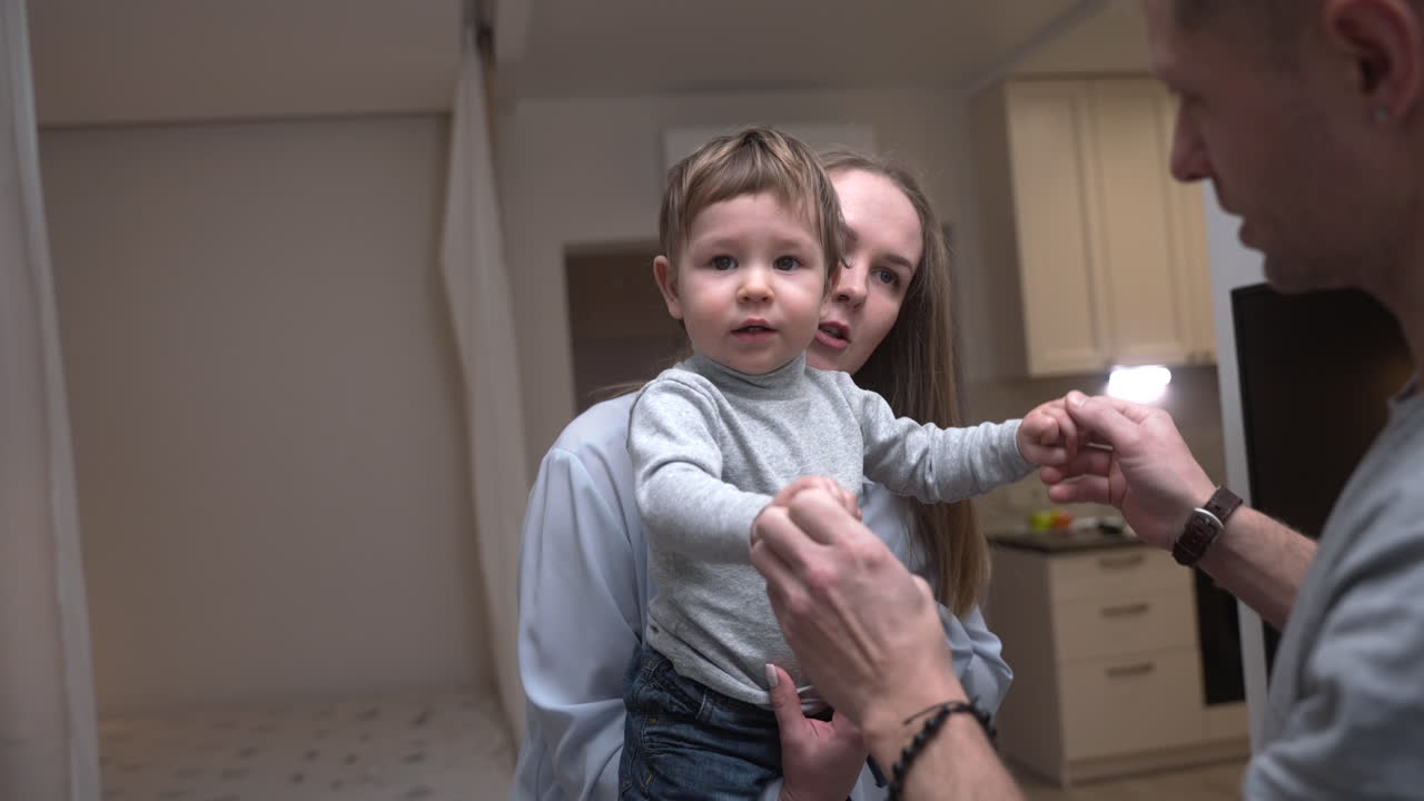 Madre che tiene in braccio il suo bambino nel soggiorno di casa, mentre il padre gli tiene le mani