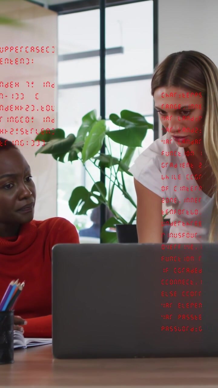 Vertical video: Women at desk collaborating, laptop showing red code overlay, starting tech review