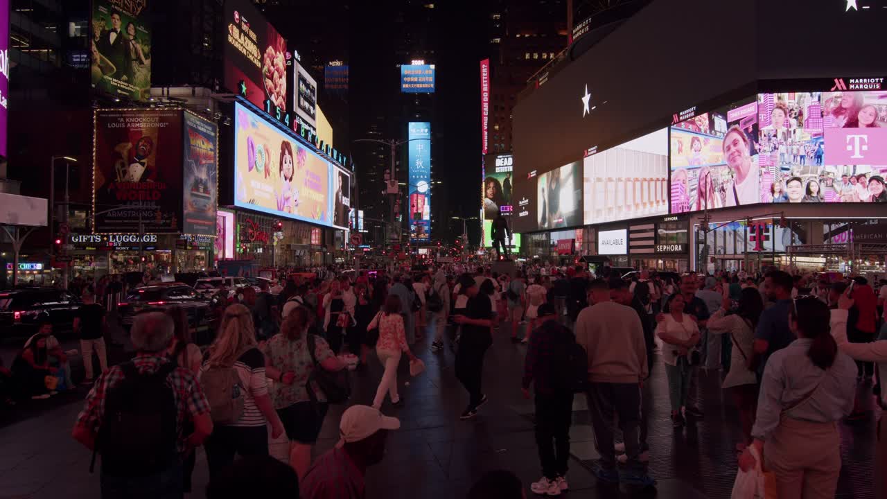 Crowds walk through Times Square at night surrounded by bright billboards and neon lights