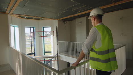 the ingineer inspects the unfinished house, stands on the second floor and looks down