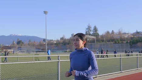 Hispanic-woman-running-on-track-and-field,-orbiting-follow-shot