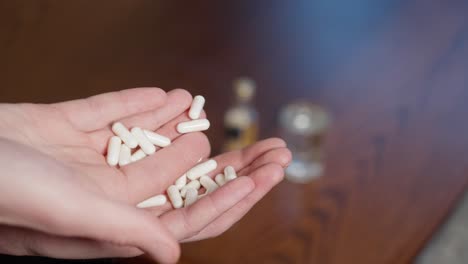 man in pain holding handful of pills in front of blurred background with alcohol, close up