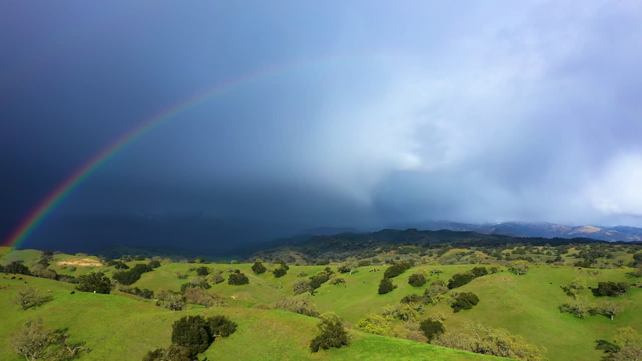 tierras de cultivo colinas con ganado con hermoso doble arco iris y montañas con nieve y tormenta tiempo drone disparado