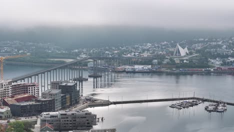 drone shot of tromso norway harbor, strait bridge and buildings in misty skyline 60fps