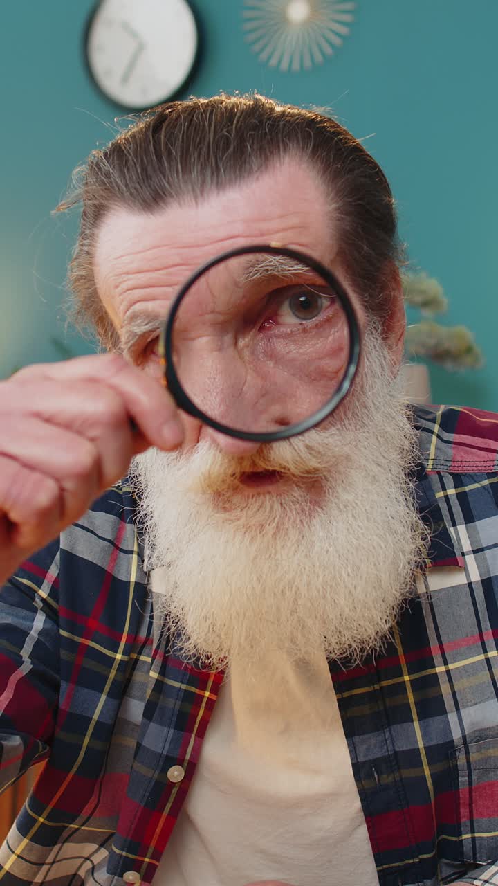 Investigator researcher scientist senior man working at home holding magnifying glass near face