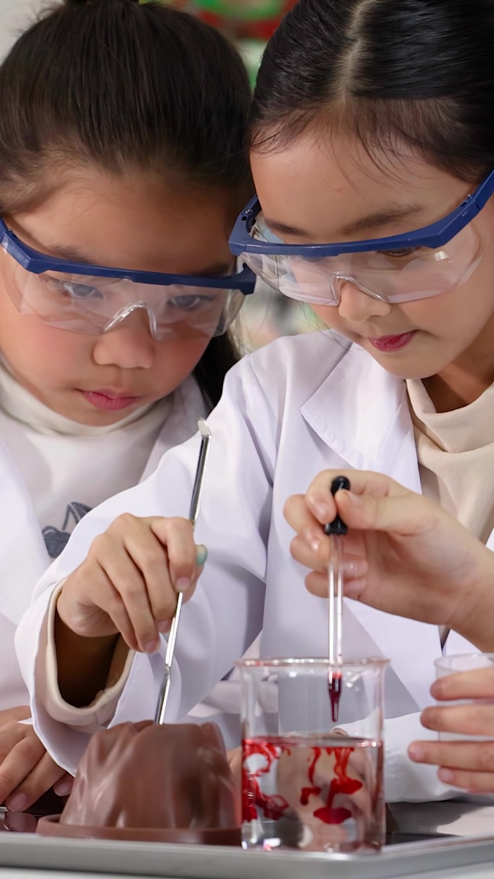 Siswa-siswi muda Asia mengenakan kacamata pengaman dan jas lab saat melakukan eksperimen sains gunung berapi.