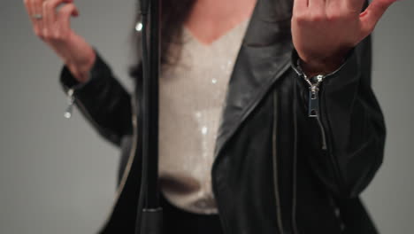 intense close-up of a faceless female vocalist in a black leather jacket gesturing with hands, camera zooming in, grey background