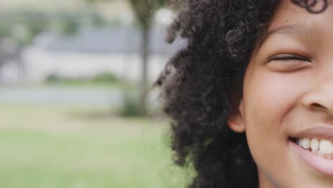 video retrato de la mitad de la cara de una estudiante biracial sonriente en el campo de juego de la escuela, con espacio para copiar