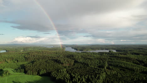 stunning rainbow over beautiful serene forest and lake landscape in finland, near kuopio, camera flying down