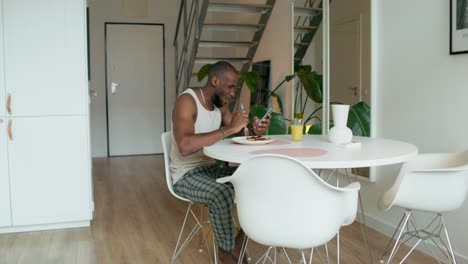 man eating breakfast and using his phone in a modern kitchen