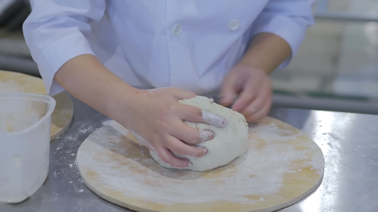 Baker hands kneading fresh dough on table at bakery - close up