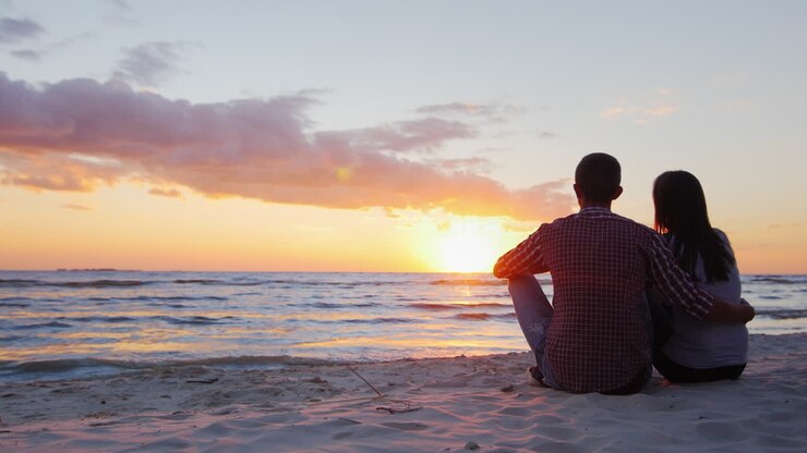 Jeune couple romantique assis sur la plage admirant le coucher de soleil.