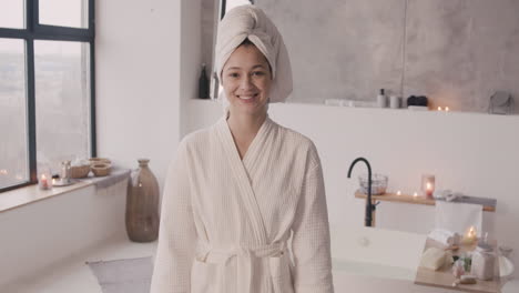 그녀의 머리와 목욕 가운에 수건으로 포즈를 취하고 카메라에 미소를 짓는 여자의 전면보기