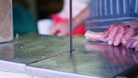 Caucasian-butcher-cuts-up-venison-leg-into-pieces-with-band-saw,-closeup