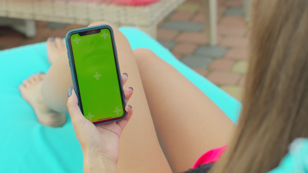 Girl using mobile phone green screen near the swimming pool. Hands holding smartphone chrome key, fingers tapping modern display smart phone.