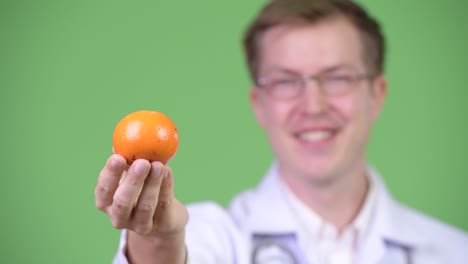 portrait of young man doctor holding orange fruit