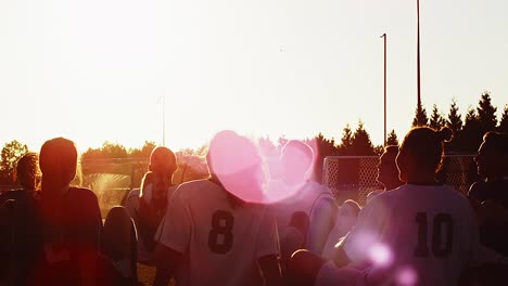 a soccer team sitting in a circle playing a fun game at sunset