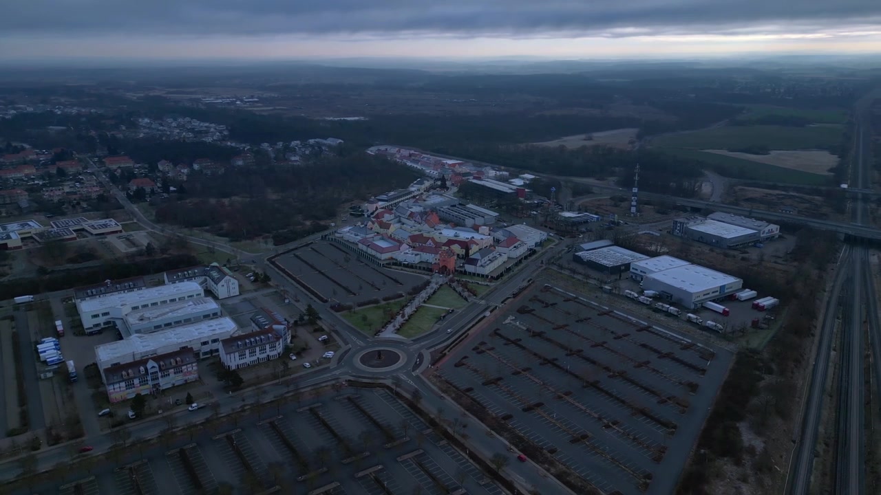 Outlet shopping center with empty parking lots, surrounding roads, roundabout and nearby railway infrastructure. Great aerial view panorama overview drone