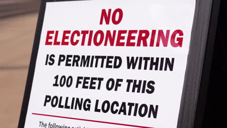 no electioneering is permitted within 100 feet of this polling location sign with person walking in background, woman