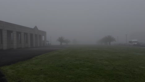 spooky view of a green field and a modern stone building covered in fog