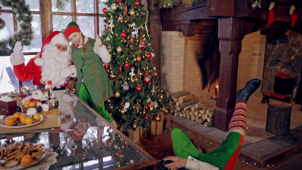 Elf boy is taking picture of Santa Claus and girl elf near the NewYear tree in decorated room. Capturing moments of happiness