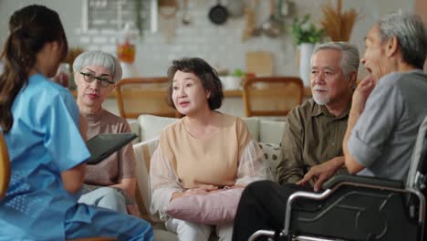 happiness cheerful elderly woman and men talking with female caregiver nurse doctor having health checking consult at living area,caretakers with senior couple sitting in living room at nursing home