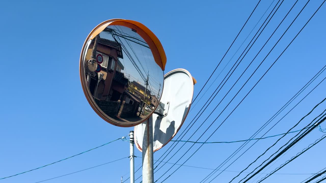 Un'inquadratura dal basso di uno specchio convesso arancione che riflette case e linee elettriche.