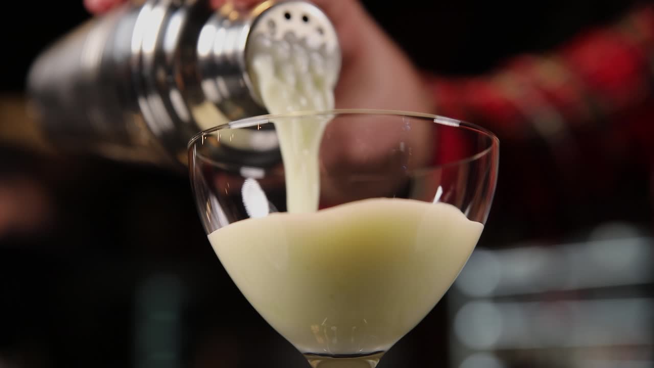 Bartender pouring a creamy cocktail into a glass