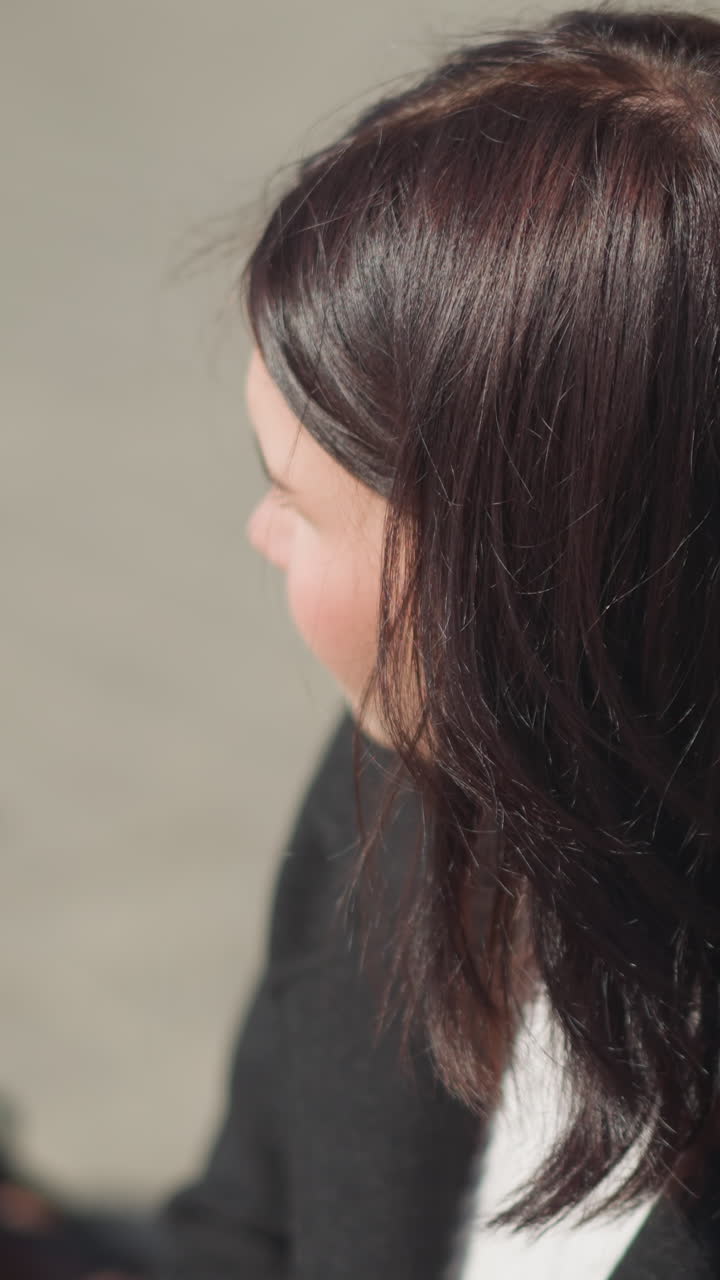 앉아있는 여자의 클로즈업, 태양 빛에 비추어 무언가에 초점을 맞추고, 머리카락이 바람에 흔들리고, 멀리보고, 불분명한 물체가 그녀의 근처에 앉아 있습니다.