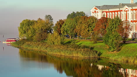 beautiful landscape near jelgava castle with boats anchored near a pierce along the river bank, and a piece of the castle seen behind the trees