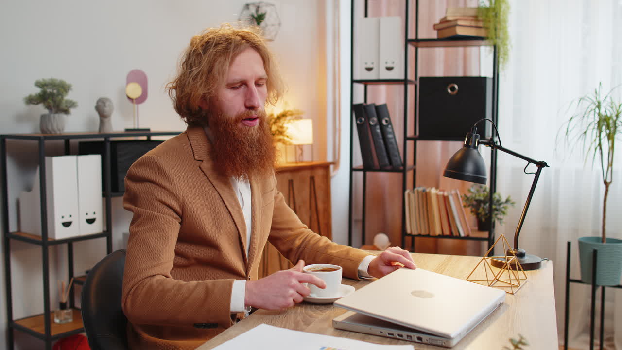 бизнесмен фрилансер дома в офисе за столом пьет утренний кофе начинает работать на ноутбуке