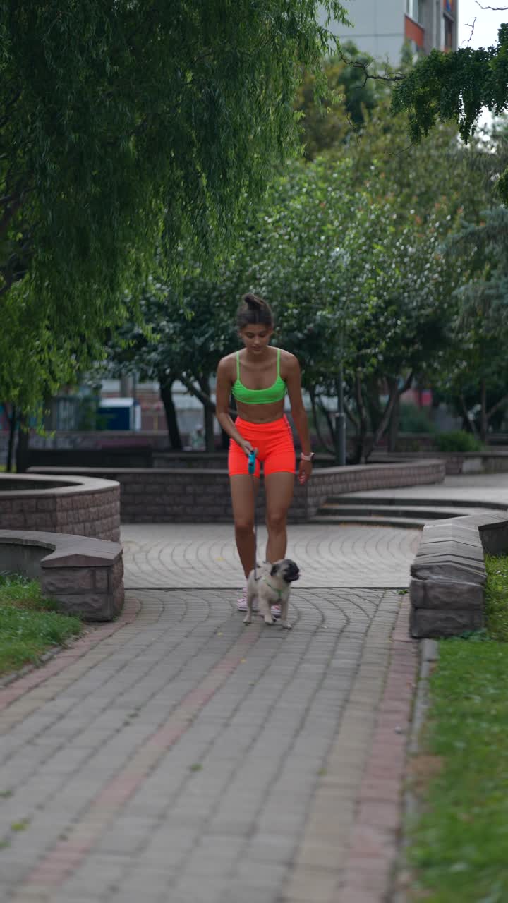 una mujer caminando con su pug en un parque.