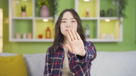 집에 있는 젊은 아시아 여성이 카메라를 쳐다보며 "멈춰"라고 말합니다.