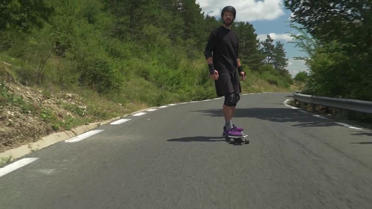 A man in protective gear skateboards along a sunny, tree-lined road, capturing a moment of outdoor adventure.