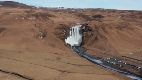 Cascada-De-Skogafoss-En-Un-Paisaje-De-Hierba-Marrón-En-La-Antigua-Costa-De-Islandia,-Antena