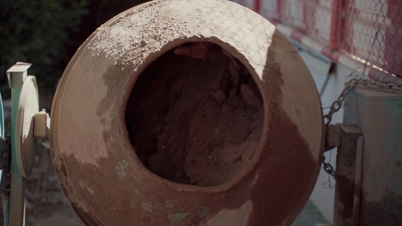Primo piano dettagliato di una betoniera rustica che mescola attivamente cemento e acqua. Attrezzatura per l'edilizia in funzione in un cantiere.