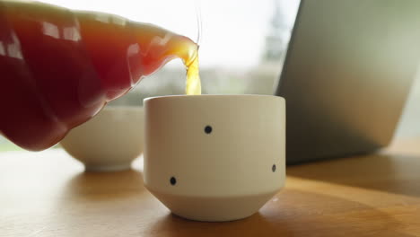 Vertiendo-Café-Recién-Hecho-En-Una-Taza-Al-Lado-De-Una-Computadora-Portátil-Y-Un-Tazón-De-Desayuno