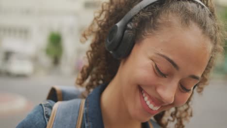 Feliz-Mujer-Birracial-En-La-Ciudad,-Usando-Audífonos-Y-Sonriendo