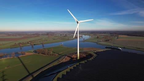 Forward-aerial-movement-approaching-single-windmill-and-solar-panel-park-in-The-Netherlands-part-of-sustainable-industry-with-intersection-of-river-IJssel-and-Twentekanaal