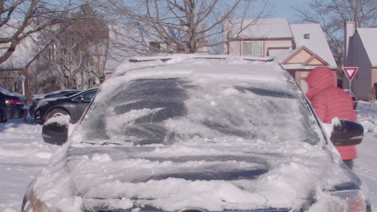 Man in orange ski jacket brushes snow off his car timelapse