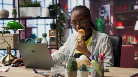 busy freelancer in home office eating snack on the go while typing on laptop